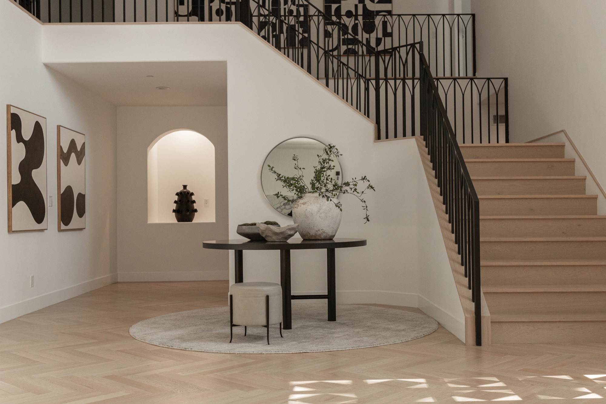 Foyer, curved staircase with a round table of ceramic vessels and art
